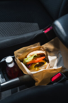 Burger in paper wrap on car seat with red drink bottle