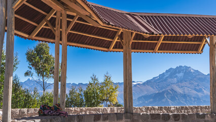 A viewing platform in the mountains. A canopy with a tiled roof, a stone fence. Mountain range, green vegetation against the blue sky. Peru.