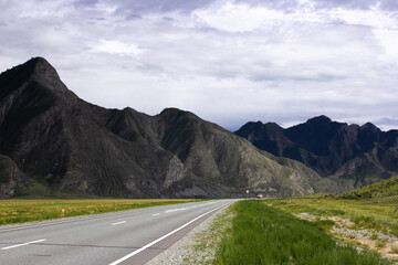 Open highway in Altai, Russia, crosses flatlands toward a striking mountain range. Captures the essence of road trips, natural freedom, and stunning Siberian scenery.