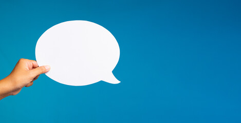 Hand holding blank round speech bubble cutout on blue background for communication and dialogue concept.