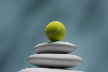 Tennis ball balanced on smooth stacked stones against blue background