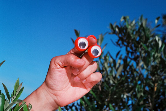 man holds a pair of red googly eyes outdoors, 35mm