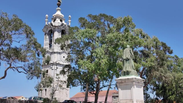 Statue and Torre Paroquial tower under clear blue sky in Lisbon Portugal with surrounding trees