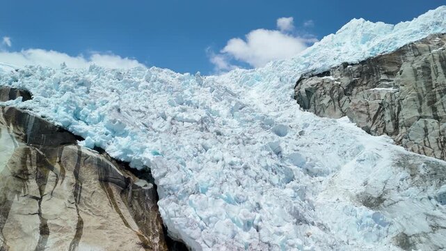 A striking aerial parallax shot reveals the frozen snow-capped peak and fractured glacier ice of Nevado Hualc&aacute;n in the Cordillera Blanca near Laguna 513