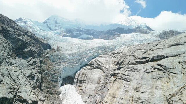A spectacular aerial drone shot rises up the face of a massive, melting glacier, revealing the vast ice fields and snow-capped peaks that feed Laguna 513 in the Peruvian Andes.