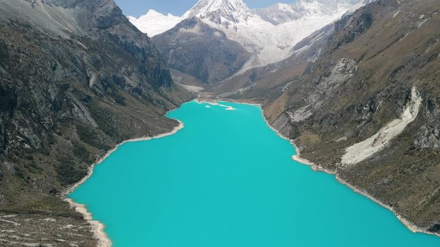 A breathtaking high-altitude aerial shot tilts up from the vibrant turquoise water of Laguna Par&oacute;n to reveal the spectacular snow-capped peaks of the Cordillera Blanca in the Peruvian Andes.