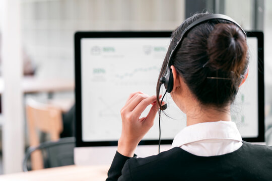 A professional customer service representative, seen from behind, wears a headset and works at a computer in a modern office
