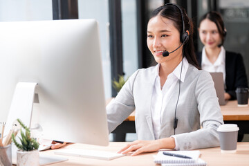 Fototapeta premium Smiling businesswoman wearing headset working on a computer in modern office.