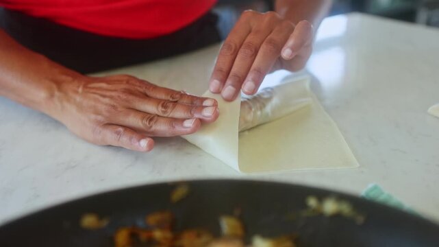 Chef preparing spring rolls with filling on kitchen counter