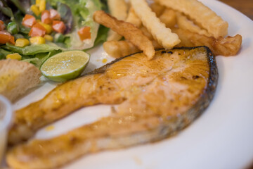 Plate of grilled salmon steak with salad and french fries. Close up