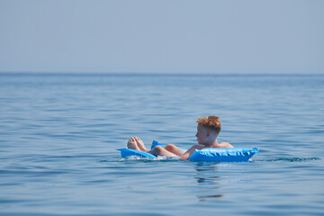 A boy chilling and resting on an air mattress in an ocean in the summer with a blue sky in the background