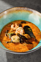 Tom yum soup with seafood in rustic bright closeup, turquoise ceramic bowl on textured surface