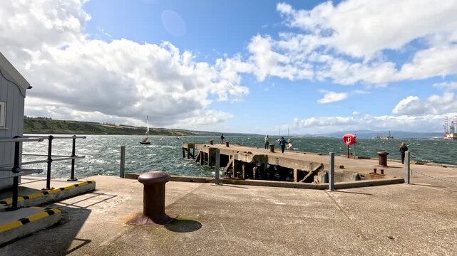 Windy Cromarty Pier with People and Sailboats Under Cloudy Sky
