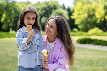 Fototapeta premium Woman and girl holding waffle cones with colorful ice cream outside