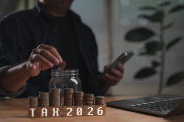 Man plans future tax 2026 obligations, saving money placing coin glass jar. Coin stacks symbolize financial growth, investment planning, managing personal budget.