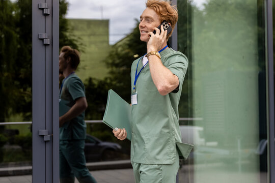 Caucasian medical worker reading patient history from folder and speaking on mobile phone