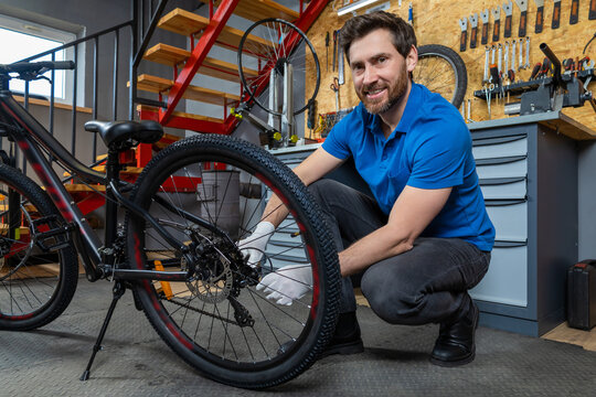 Bicycle mechanic in blue shirt kneeling with gloves adjusting cycle tire in organized indoor garage
