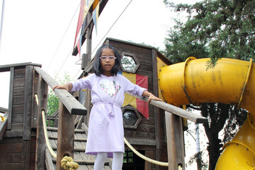 5-year-old Latina brunette girl with glasses plays on public playground equipment alone as therapy for ADHD