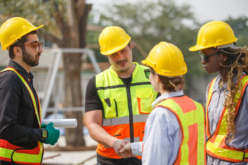 Diverse construction team wearing safety helmets and reflective vests shaking hands at building site symbolizing teamwork, agreement, partnership and successful project collaboration.