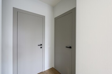 Two closed doors, light and dark gray, in a white hallway. Modern interior with minimal design. Black handles