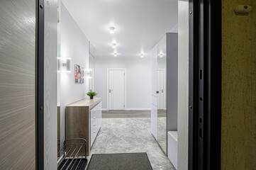 modern entryway with gray marble floors, a white door at the end of the hallway, mirrored closet doors on the right, and a dresser on the left