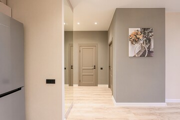 modern hallway with beige walls, light wood floors, and neutral doors.  A bicycle picture hangs on the wall. A fridge is partially visible