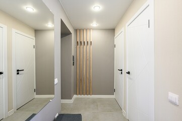modern hallway with white doors, gray walls, tile flooring, and a wooden coat rack. Minimalist design