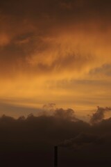 Industrial smokestack emitting dark smoke against a dramatic orange and gold sunset sky, symbolizing air pollution, environmental impact, and climate change awareness