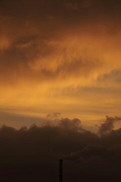 Industrial smokestack emitting dark smoke against a dramatic orange and gold sunset sky, symbolizing air pollution, environmental impact, and climate change awareness