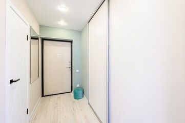 bright hallway features white doors, walls, a wardrobe with sliding doors, and light wood flooring. A mirror and a teal ottoman add a touch of color