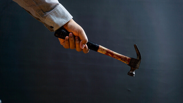 Man in long-sleeved shirt gripping hammer’s black rubber handle, black background, ideal for repair, construction, or handyman concepts.