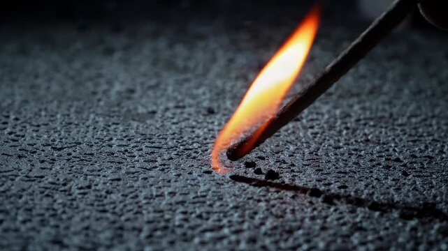 Scientist carefully burning wooden matchstick against dark asphalt, revealing glowing embers trailing across textured surface with intense heat and fiery combustion