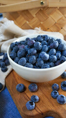 A bowl of ripe blueberries sits on a wooden board with a woven basket in the background, creating a rustic and natural setting ideal for showcasing healthy, fresh, and organic food. Close up
