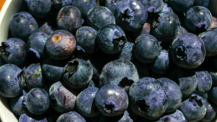 A bowl of ripe blueberries sits on a wooden board with a woven basket in the background, creating a rustic and natural setting ideal for showcasing healthy, fresh, and organic food. Close up