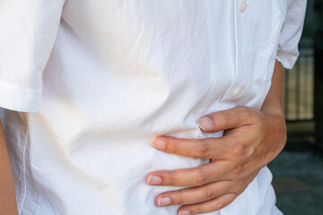 An Asian man clutching their abdomen in sharp pain in a clinical setting, highlighting stomach, intestinal, and visceral distress—ideal for digestive treatment ads.