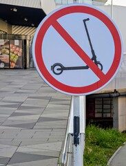 Close-up photo of a No Electric Scooters Allowed sign placed in an urban pedestrian area near a shopping mall entrance