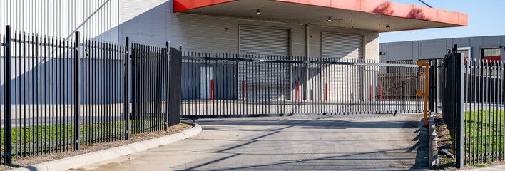 Secure industrial facility entrance with metal security fencing and an automated sliding gate, leading to a loading dock, commercial property, warehouse or factory