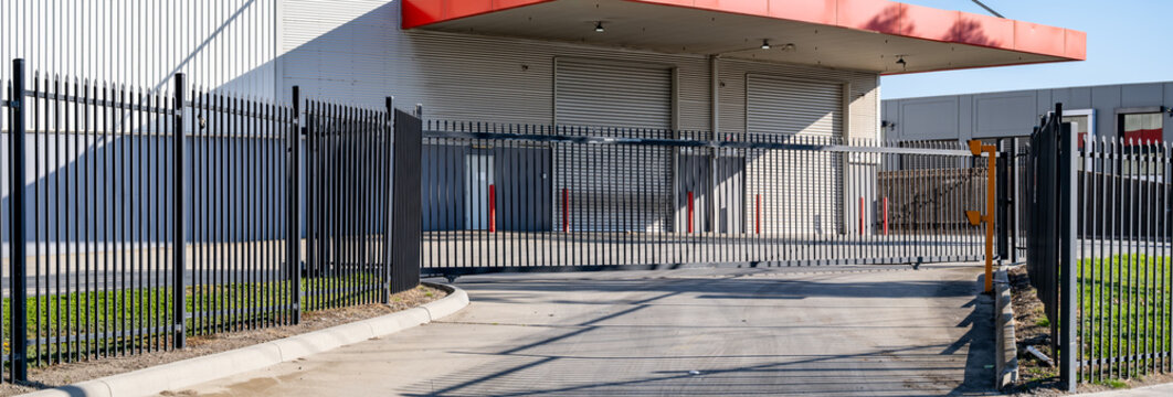 Secure industrial facility entrance with metal security fencing and an automated sliding gate, leading to a loading dock, commercial property, warehouse or factory
