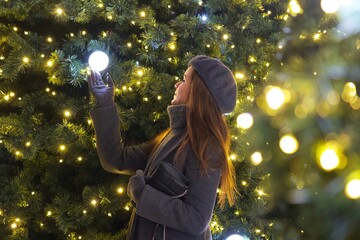 Naklejka premium Elegant Parisian girl near Christmas tree gazing at festive decorations