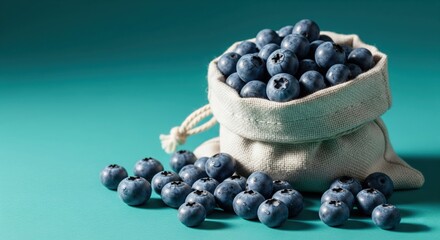 Fresh blueberries spilling from a canvas bag on a teal background