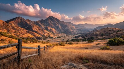 Golden hour illuminates a vast valley, mountains in background, split rail fence foreground