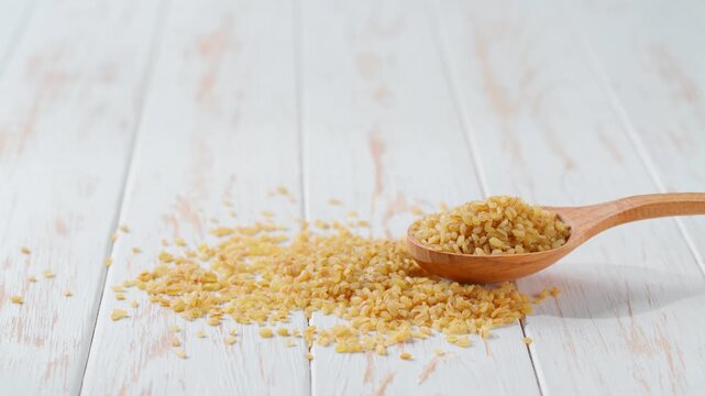 bulgur in a wooden spoon on a white kitchen table.
Raw bulgur in a wooden spoon on a light kitchen table.