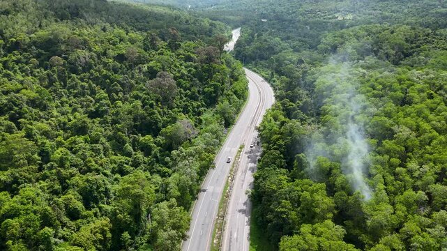 Drone footage of the aerial view of a winding road cutting through lush green forest. Scenic highway number 304 in Thailand links the Bangkok area to Nakhon Ratchasima in the northeastern region
