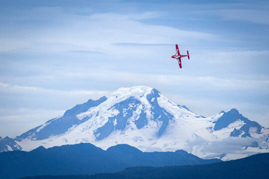 olo aerobatic jet banks sharply before a glaciated peak under soft blue clouds, a clean aviation scene conveying speed, precision, ambition and modern power against a wild mountain backdrop.