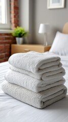 Close-up of a stack of fluffy white towels on a fresh, white bed in a cozy home bedroom. 
