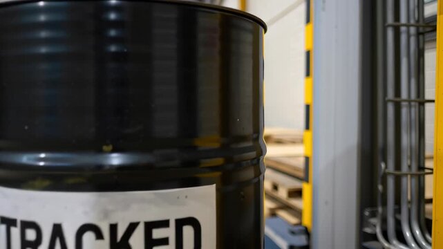 Untracked black metal barrel in industrial warehouse with shelving, safety sign, and risk markings highlighting storage and regulation concerns