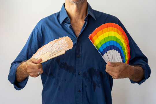An unrecognizable man in a blue shirt sweats while
fanning himself with two fans, one of them in the colors of the LGBTI community