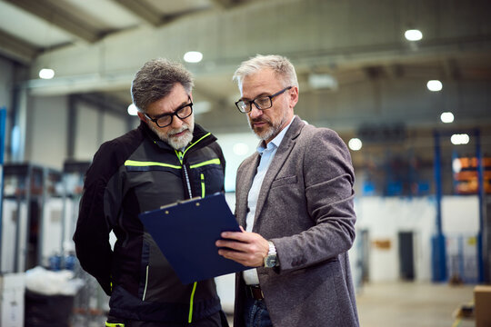 Warehouse Workers Reviewing a Clipboard Document in a Work Environment