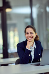 Obraz premium Confident Businesswoman Smiling at Desk With Laptop in Modern Office Setting