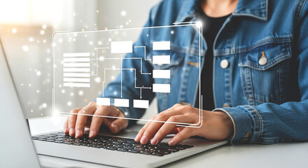 Person typing on a laptop with a digital flowchart overlay and wearing a blue denim jacket indoors